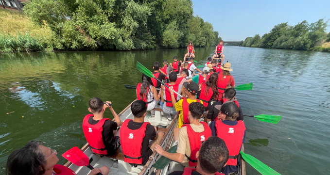 Die Teilnehmenden der Jugendbegegnung sitzen in Schwimmwesten auf einem Boot und rudern