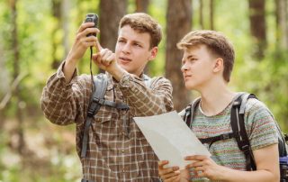Zwei Personen stehen im Wald und betrachten gemeinsam eine Karte und ein GPS Gerät