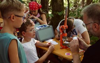 Mädchen und Jungen gestalten beim "Inklusiven Zeltlager" mit ihrem Betreuer Philipp Steinert an einer Biertischgarnitur bunte Buttons.