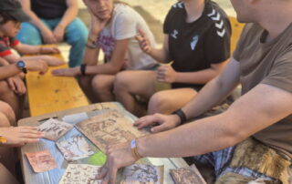 Eine Gruppe sitzt mit ihren Betreuern beim Lagerspiel zusammen und löst eine Aufgabe zum Thema "Höhlenmalerei".