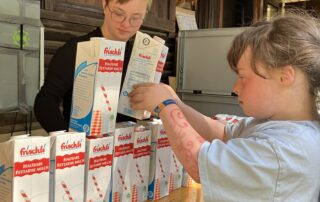 Zwei Mädchen bauen beim "Inklusiven Zeltlager" eine Tetrapack-Pyramide zum "Dosenwerfen".