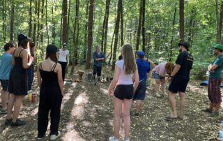 Teilnehmende vom "Inklusiven Zeltlager" stehen im Wald und machen mit Klaus Neubert einen Rhythmus-Workshop.