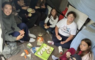 Dem Regenwetter trotzend sitzt eine Mädelsgruppe vom "Inklusiven Zeltlager" gemeinsam mit ihren Betreuerinnen in einem Bus und macht Picknick.