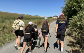Eine Mädelsgruppe schiebt beim Wandertag des "Inklusiven Zeltlagers" einen Rollstuhl.
